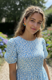 Close-up of woman wearing colour-block heart stud earrings outdoors in a garden setting