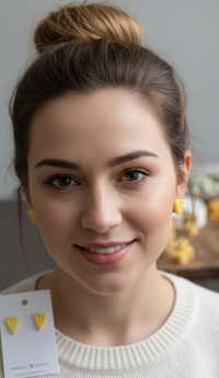 Close-up of a woman wearing small yellow cheese stud earrings with hair in a bun