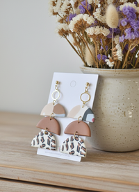 Clay tiered leopard print earrings displayed on card beside dried flower arrangement