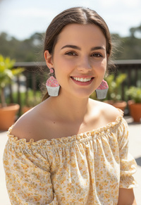 Model wearing pink cupcake drop earrings with off-shoulder floral top, side view