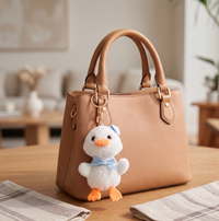 White sailor duck plush keychain clipped to tan leather handbag, front view