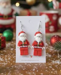 Two acrylic Santa figure drop earrings on a white card with festive background