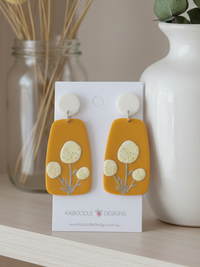 Mustard perspex drop earrings with cream speckled billy button flower design on card