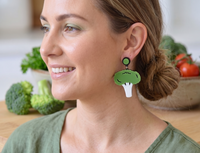 Close-up side view of broccoli earring worn on model's ear, showing white stalk and green floret detail