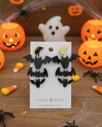Black glitter bat and gold moon drop earrings on a Kaboodle Designs card, styled with Halloween pumpkins