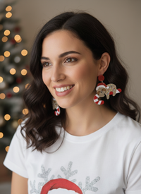 Woman wearing sloth Santa candy cane earrings, close-up side view with Christmas tree lights in background