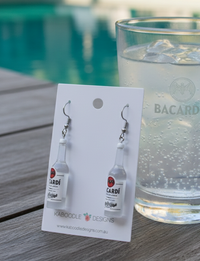 Resin rum bottle drop earrings on a Kaboodle Designs card beside a glass