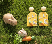 Mustard drop earrings shown beside small toy rabbit and carrot figurines on grass