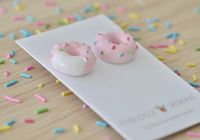 Close-up of two resin donut stud earrings with pink icing and sprinkles on wooden table