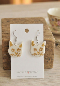 White Perspex cat face drop earrings with gold heart ears on Kaboodle Designs card