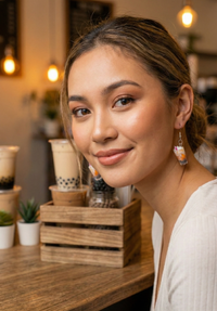 Close-up of a woman wearing a resin milkshake earring, styled against a boba shop backdrop