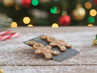 Pair of gingerbread man earrings lying flat on snowy tabletop with candy canes