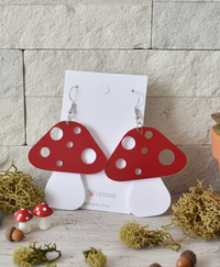 Pair of red and white spotted mushroom acrylic earrings on a white display card