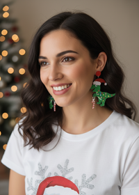 Woman wearing green glitter Christmas dinosaur earrings with Santa hat and candy cane detail