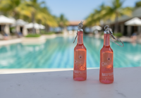 Close-up of Vodka Cruiser raspberry bottle earrings hanging against a blurred pool background
