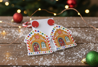 Close-up of gingerbread house earrings on wooden table with fairy lights and snow-effect styling