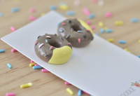 Close-up of two chocolate donut stud earrings showing bitten yellow cake edge and glossy resin glaze