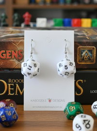 White D20 dice earrings with black numbers, on Kaboodle Designs card against fantasy game boxes