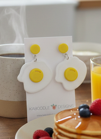 White and yellow perspex fried egg drop earrings displayed on a Kaboodle Designs card