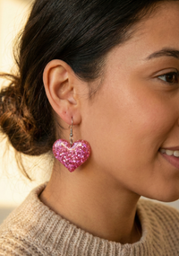 Close-up of hot pink glitter heart earring worn on model's ear