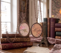 Two oval resin pendant necklaces on antique bronze chains, one showing a pink rose, one showing 'Hope' script