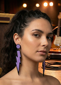 Close-up of purple lightning bolt earring worn on ear, showing glossy glitter finish and black outline