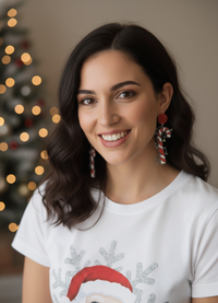 Woman wearing red glitter and candy cane drop earrings, smiling in front of a Christmas tree