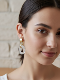 Gold-toned faceted circle drop earring worn on model's ear, close-up angle