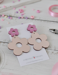 Pink flower drop earrings on card laid flat among pastel beads and pink ribbon