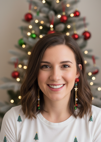 Woman wearing long Christmas charm drop earrings with red bow and bell detail, styled against a Christmas tree