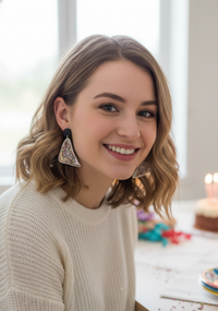 Woman wearing colourful sprinkle fairy bread earrings with a birthday cake in the background