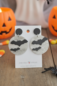 Acrylic bat and moon drop earrings on a Kaboodle Designs card, styled with Halloween pumpkins and candy corn