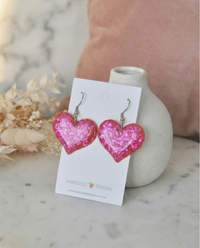 Pair of glitter heart drop earrings on branded card, angled view showing sparkle