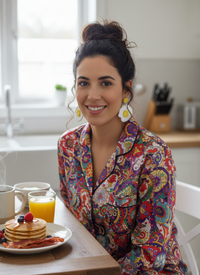 Woman wearing sunnyside egg dangle earrings while smiling at a breakfast table