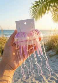 Hand holding pair of jellyfish dangle earrings on card showing bell shape and long tentacles