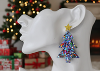 Close-up of glitter Christmas tree earring worn on ear, shown against festive background