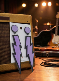 Pair of purple glitter lightning bolt Perspex earrings on card, propped against a guitar amp