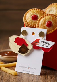 Acrylic meat pie and tomato sauce drop earrings on a Kaboodle Designs card, shown beside a pie box and chips