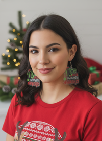Close-up of model wearing Nice Until Proven Naughty acrylic earrings against festive background