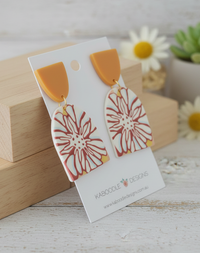 Angled view of geometric flower statement earrings on display card beside daisies