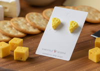Cheese wedge stud earrings on a display card beside crackers and cheese cubes