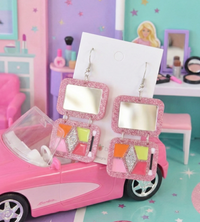 Pink palette earrings displayed against Barbie dream house scene with pink car and dressing table
