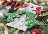 Close-up angled view of Christmas T-rex earrings showing glitter finish, fairy lights print and candy cane charm