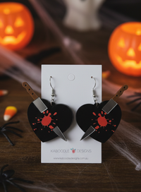 Black heart-shaped acrylic earrings with knife through centre and red blood splatter, on Kaboodle Designs card with