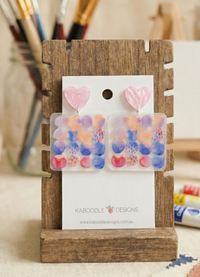 Pastel heart stud and geometric dot drop earrings displayed on a Kaboodle Designs card against a wooden stand