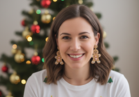 Woman wearing gingerbread man drop earrings in front of a Christmas tree
