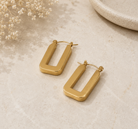Pair of gold rectangle hoop earrings laid flat on stone surface with dried flowers