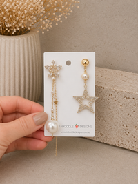 Mismatched gold-toned star earrings on card, one long pearl chain drop and one pavé star