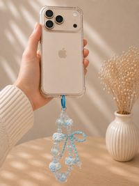 Hand holding phone with blue and clear beaded bow charm clipped to clear case