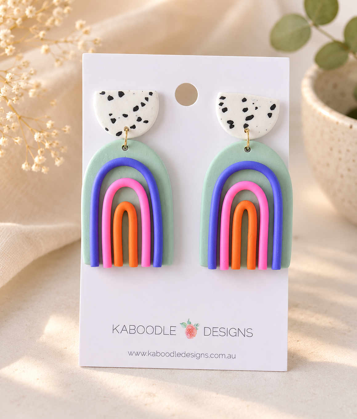 Clay rainbow drop earrings on card, speckled white tops with sage, blue, pink and orange arches